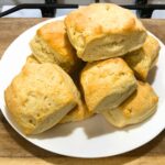 Homemade biscuits on a white plate sitting on a wooden cutting board.
