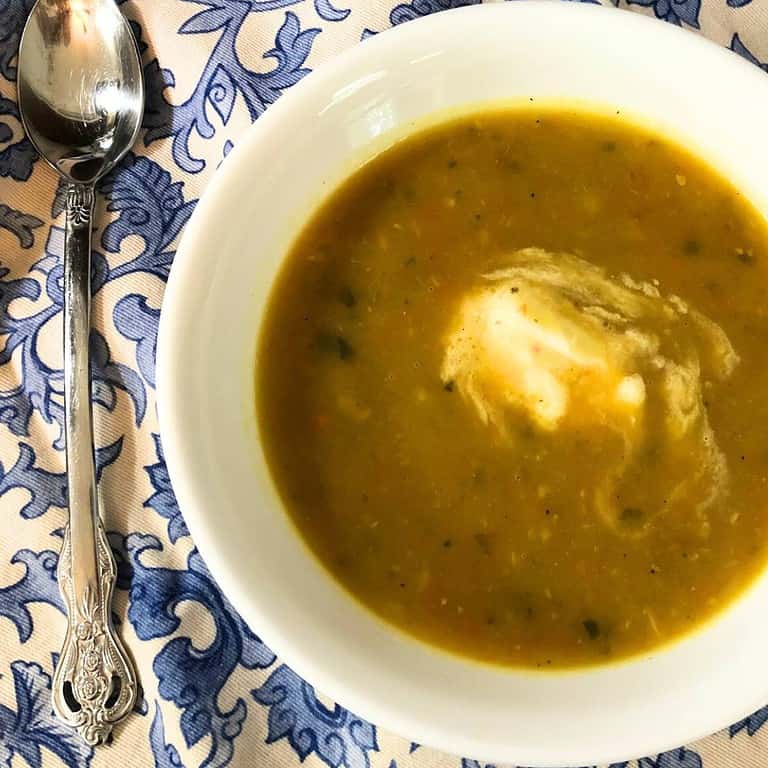 White bowl of creamy vegetable soup on a blue and white paisley tablecloth.