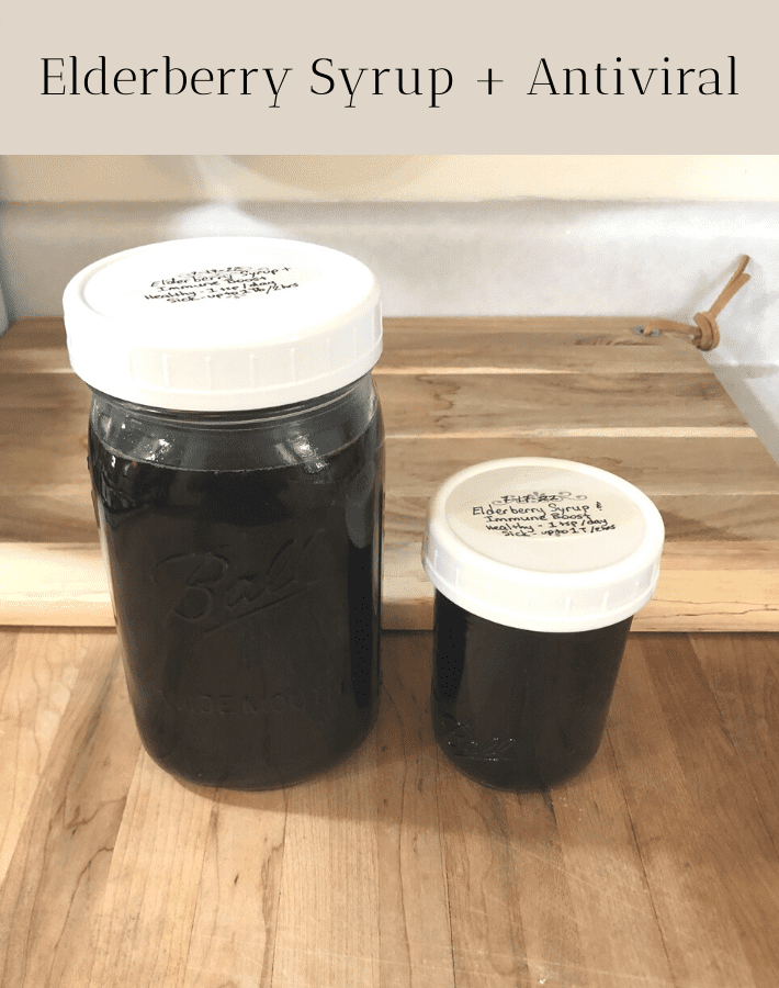 Quart jar and half-pint jar of elderberry syrup with antiviral sitting on a wooden cutting board on a counter.