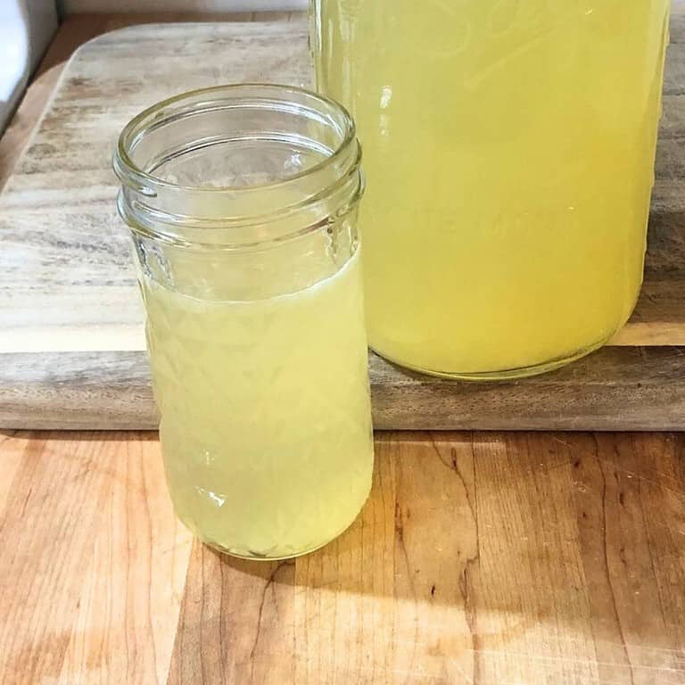 A half-gallon mason jar full of healthy honey lemonade next to a pint jar full of healthy honey lemonade, all sitting on a wooden cutting board.