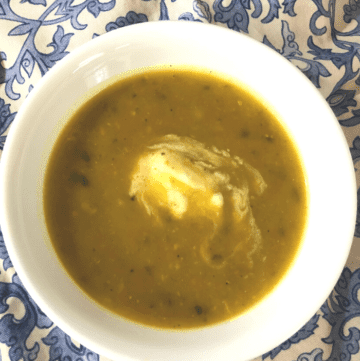 White bowl of creamy vegetable soup on a blue and white paisley tablecloth.