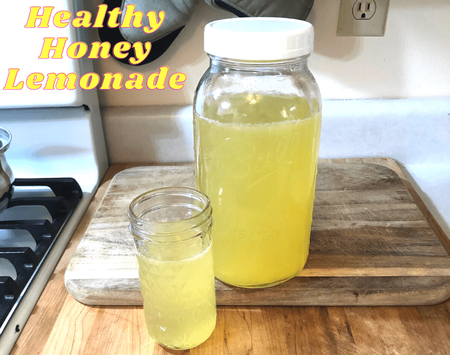 Half-gallon mason jar and small jar filled with healthy honey lemonade, sitting on wooden cutting boards on a counter.