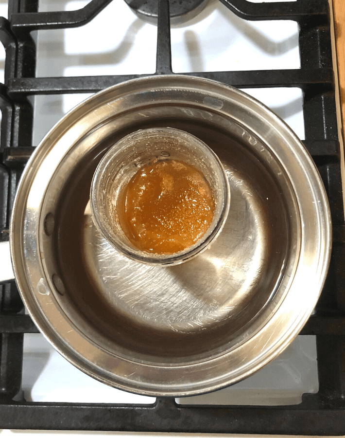 Jar of crystallized honey inside a pot of water on the stove.