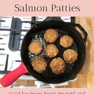 Seven healthy salmon patties cooking in a cast iron skillet on the stove.