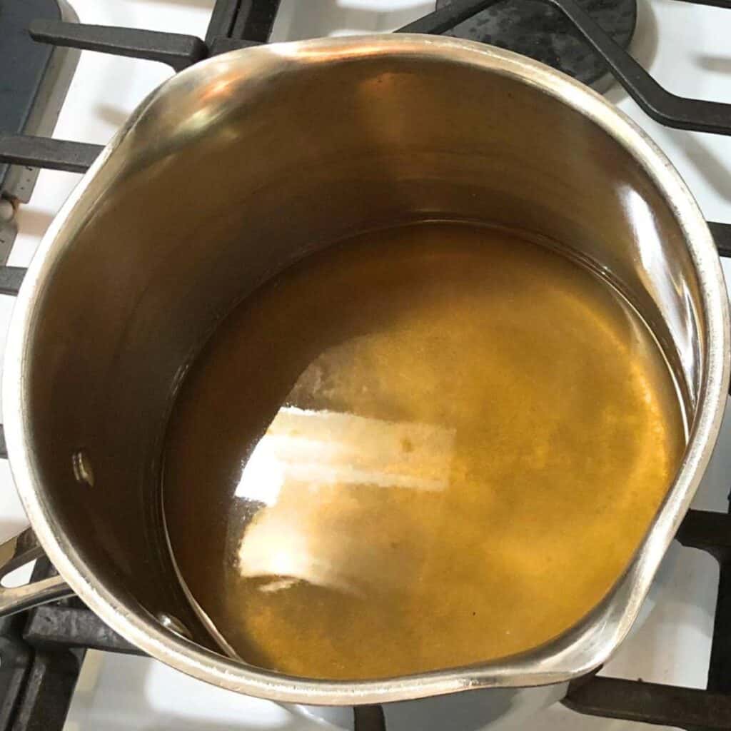 A medium saucepan on a gas stove with sugar water inside.