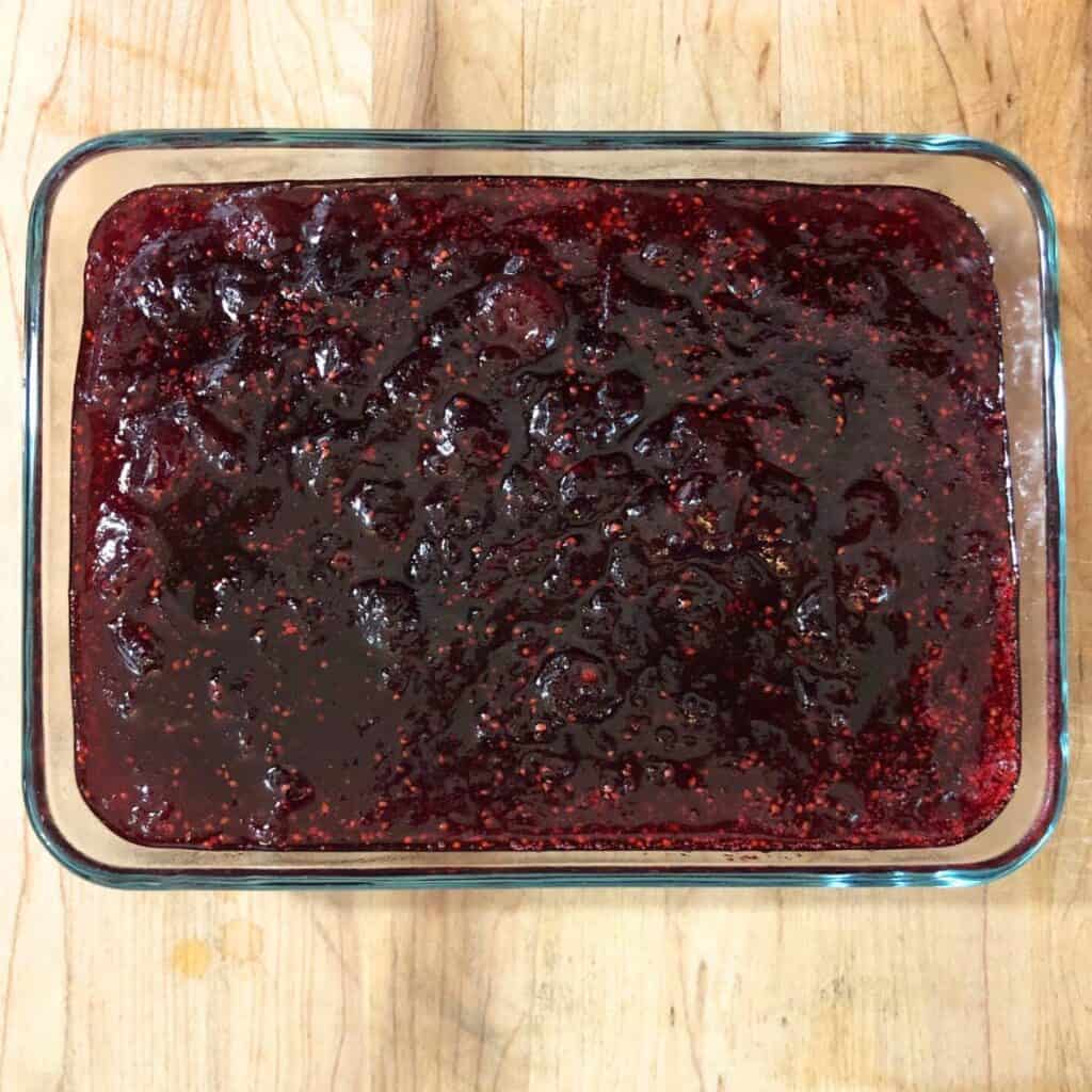 Molded cranberry sauce in a glass dish sitting on a wooden kitchen counter. 