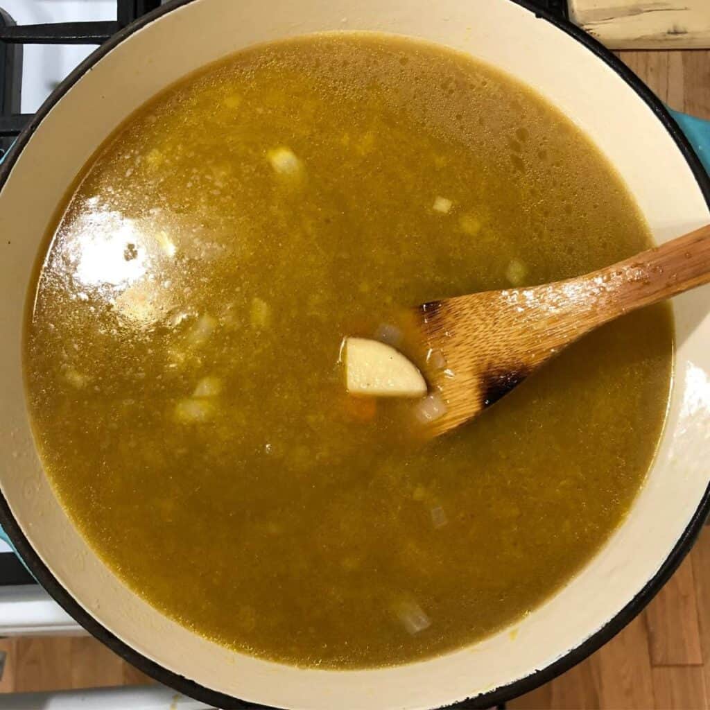 Woman stirring vegetable soup in a turquoise Dutch oven.