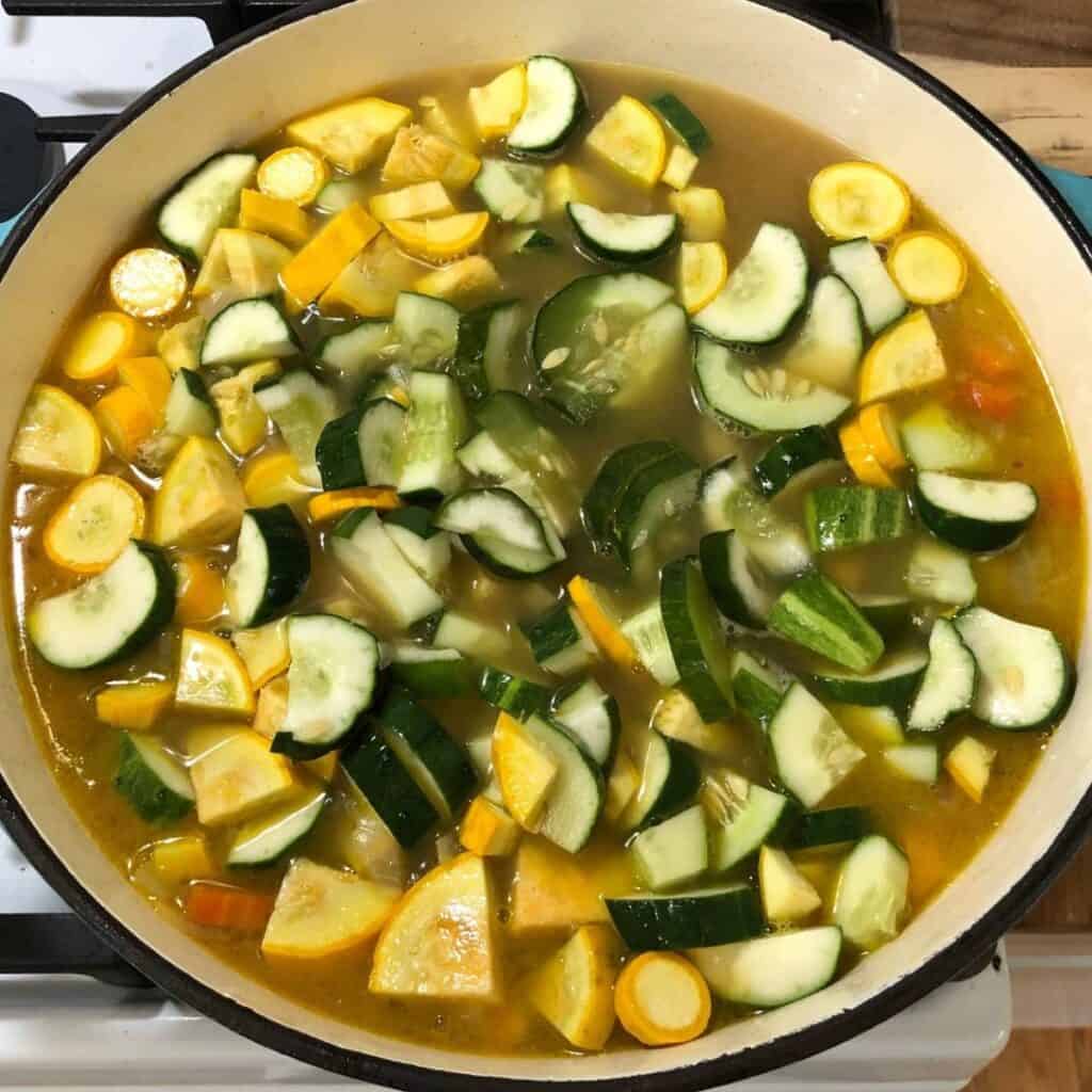 A turquoise Dutch oven with diced vegetables in chicken bone broth, cooking on the stove.