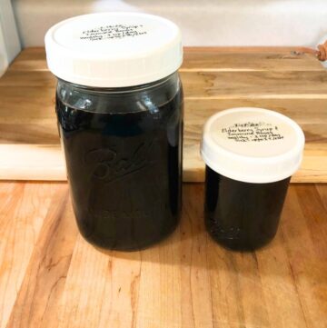 Two glass mason jars of elderberry syrup sitting on a wooden cutting board.