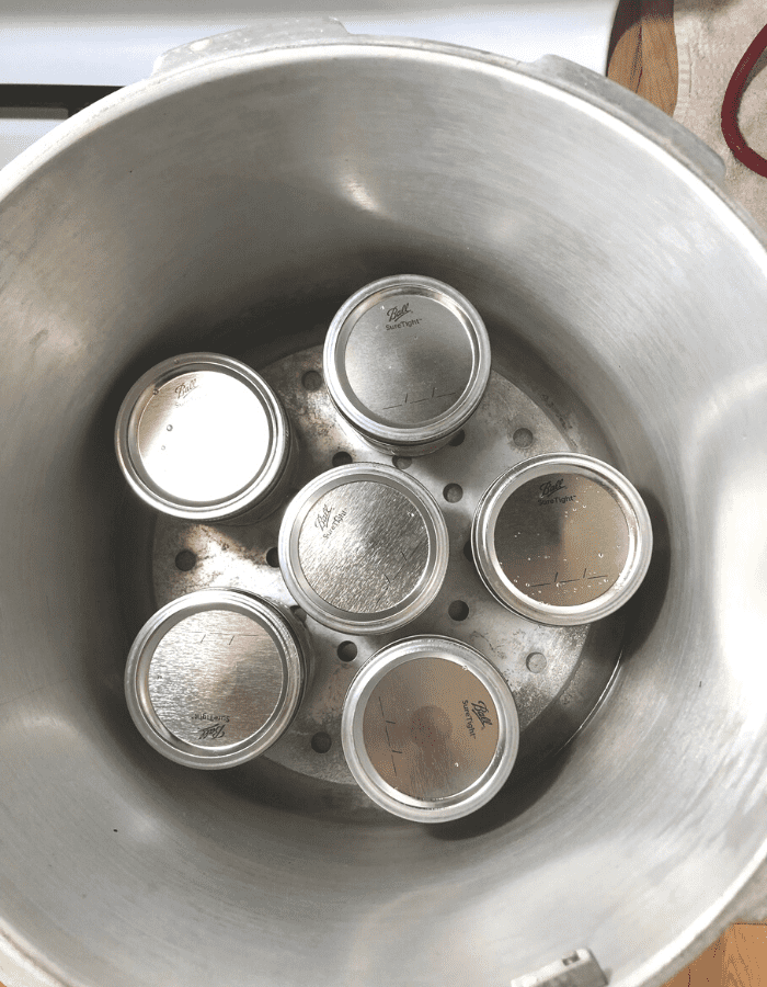 Overhead view of pressure canner with six pint jars of canned chicken.