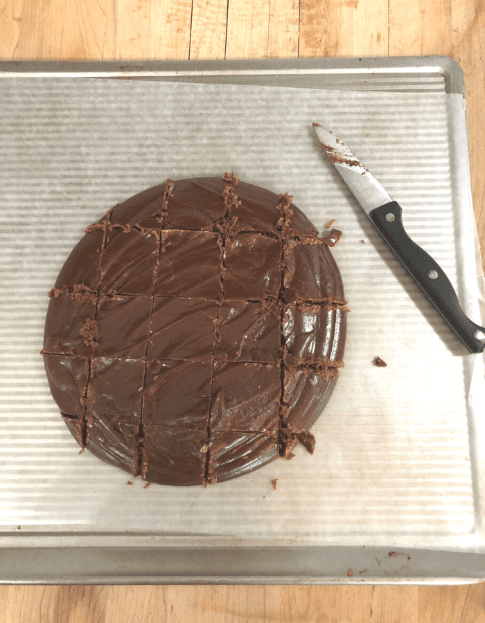 Old-fashioned chocolate fudge on a cookie sheet lined with wax paper and the fudge has been cut into squares using a sharp knife off to the side.