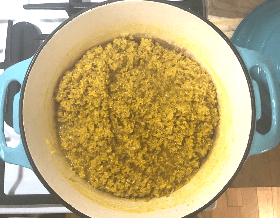 A turquoise dutch oven on a stove with yellow rice inside.