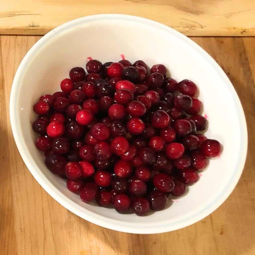 A white bowl with red cranberries inside.