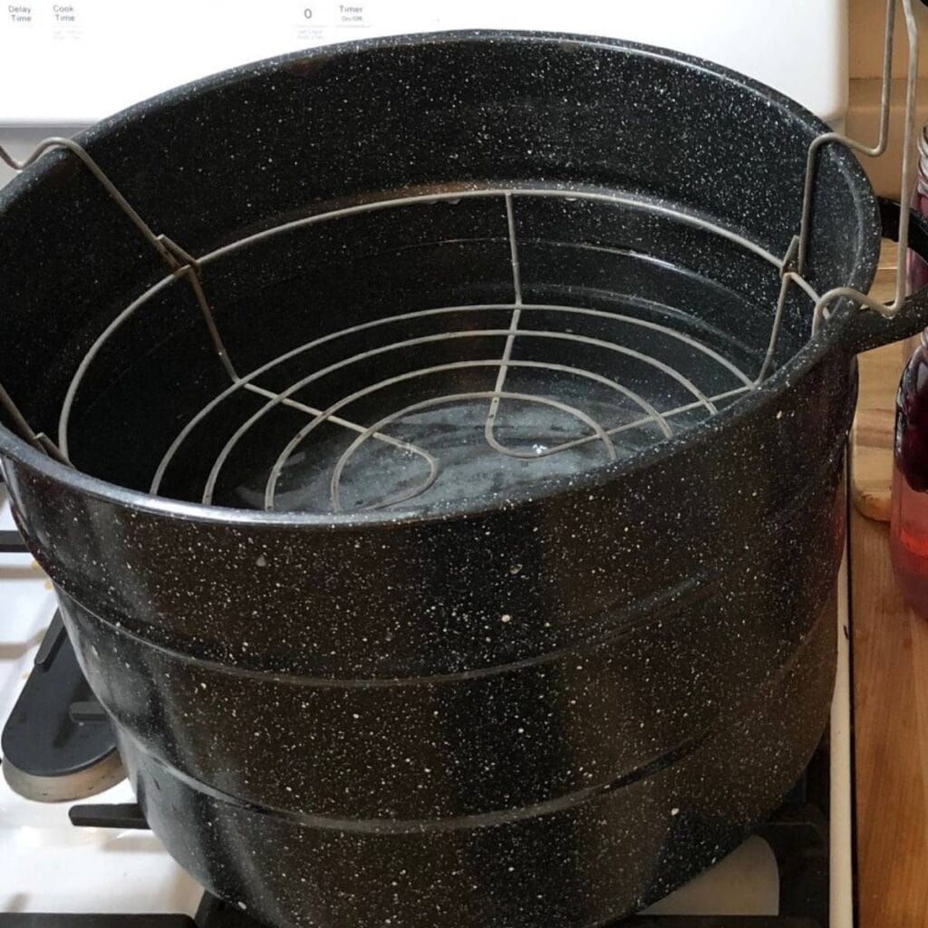 A water bath canner sitting on top of a stove. The jar rack is inside the canner.