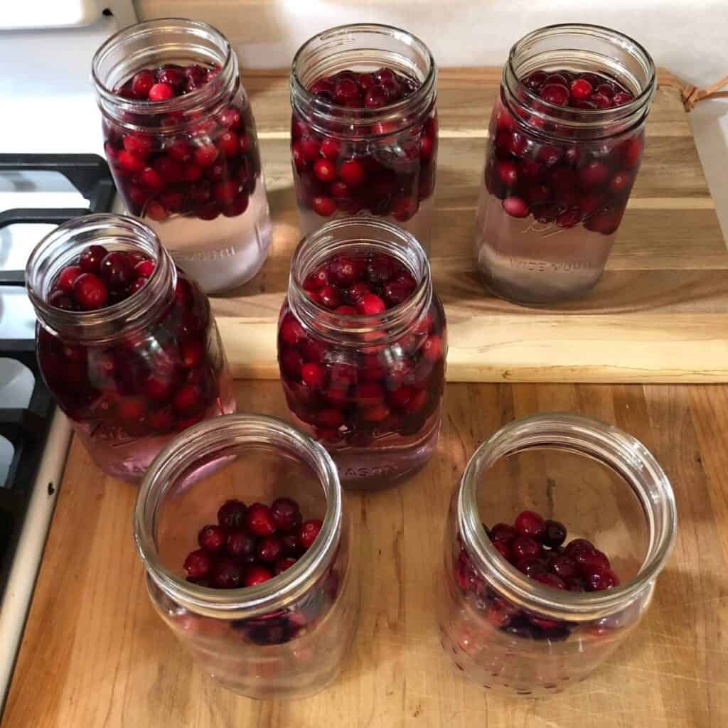 Quart mason jars filled about half way with cranberries, and the rest of the way with water, sitting on a wooden cutting board.