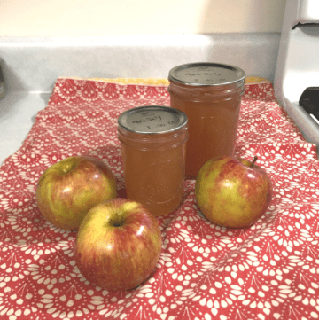 Two mason jars of apple jelly next to three red apples.