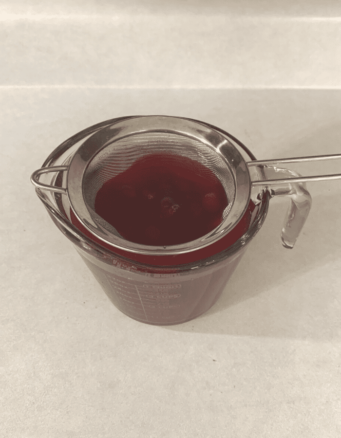 Cranapple juice in a large measuring cup with a fine mesh sieve over the top straining out the cranberries.