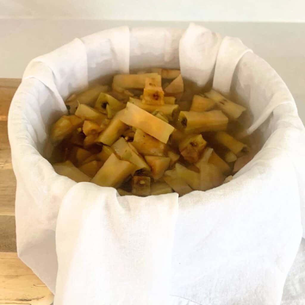 Woman pouring steaming apple cores inside a large bowl with a white flour sack towel inside.