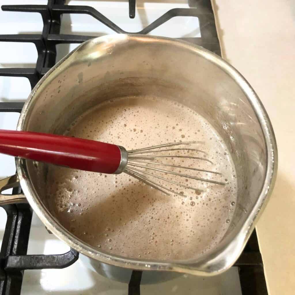 Woman whisking apple juice in a medium pot on the stove.