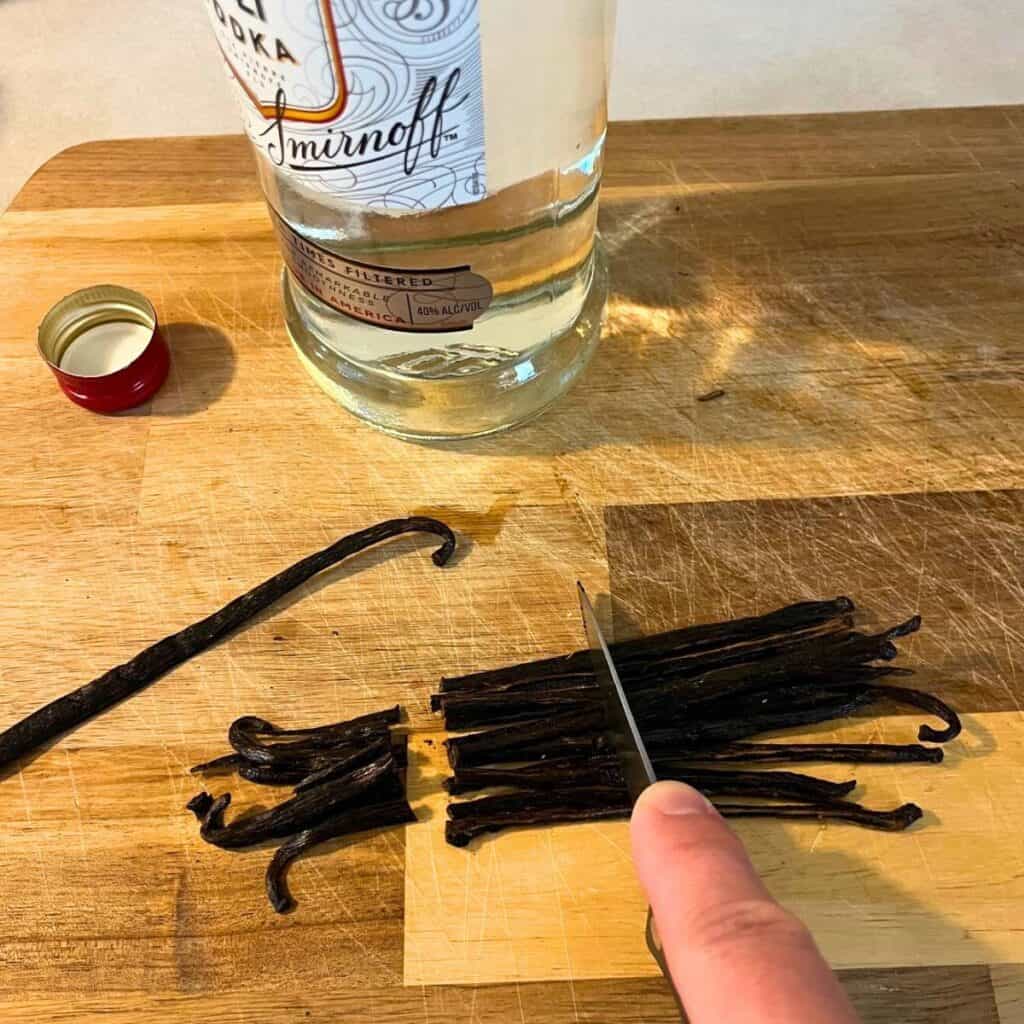 Woman cutting vanilla beans on a wood cutting board next to a bottle of Smirnoff vodka.