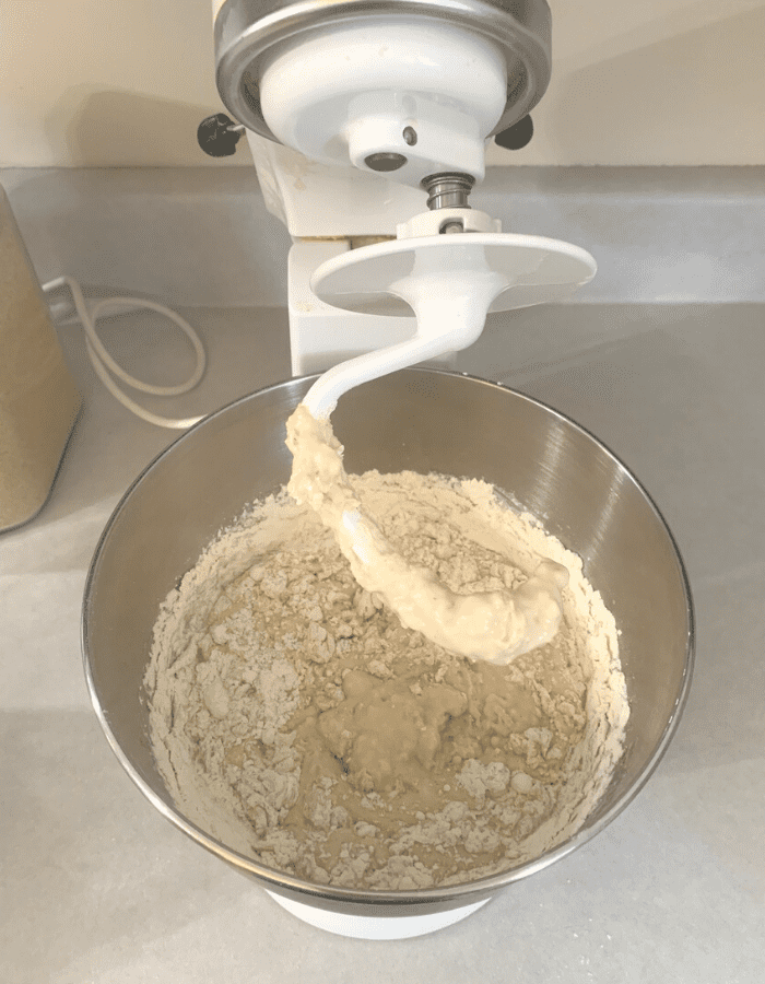 A white stand mixer with dough hook attachment mixing ingredients for sandwich bread.