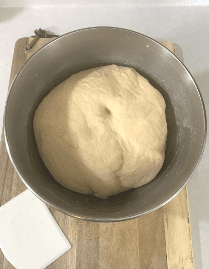 A stainless steel mixing bowl with bread dough inside.