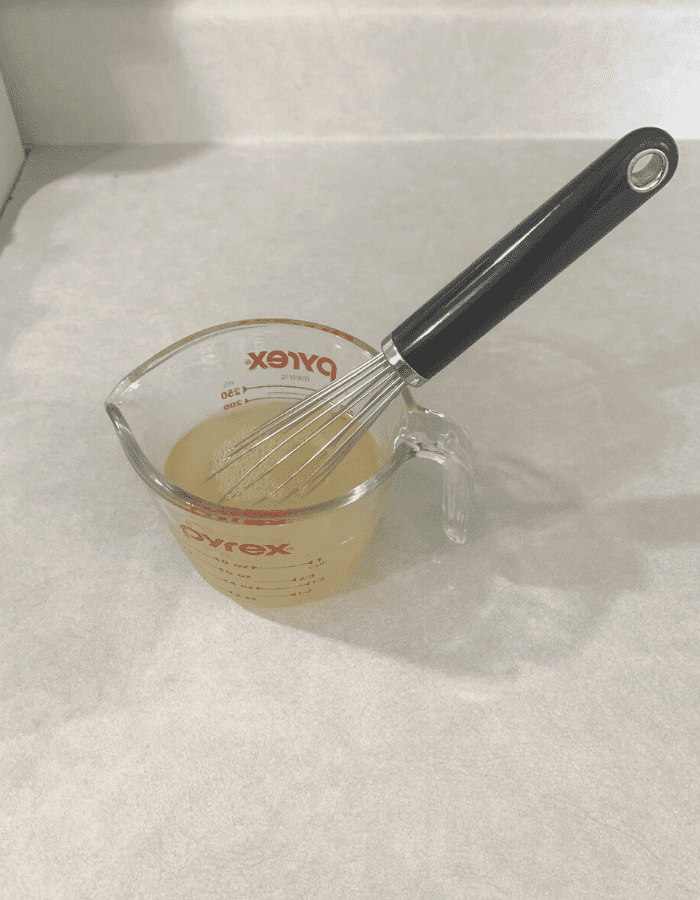 A glass measuring cup with water and beef gelatin mixed in with a whisk.