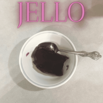 A white bowl sitting on a counter with cherry jello inside along with a silver spoon