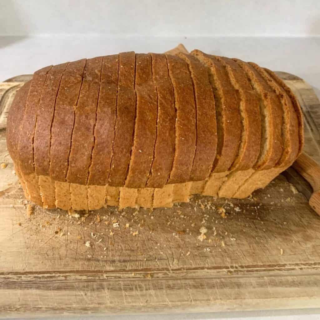 A freshly made loaf of easy sandwich bread on a wooden cutting board. The loaf has been sliced thin with a fiddle bow bread knife.