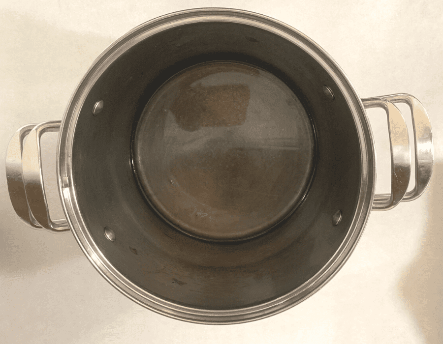 A stainless steel pot with a couple inches of water in the bottom, sitting on a kitchen counter.