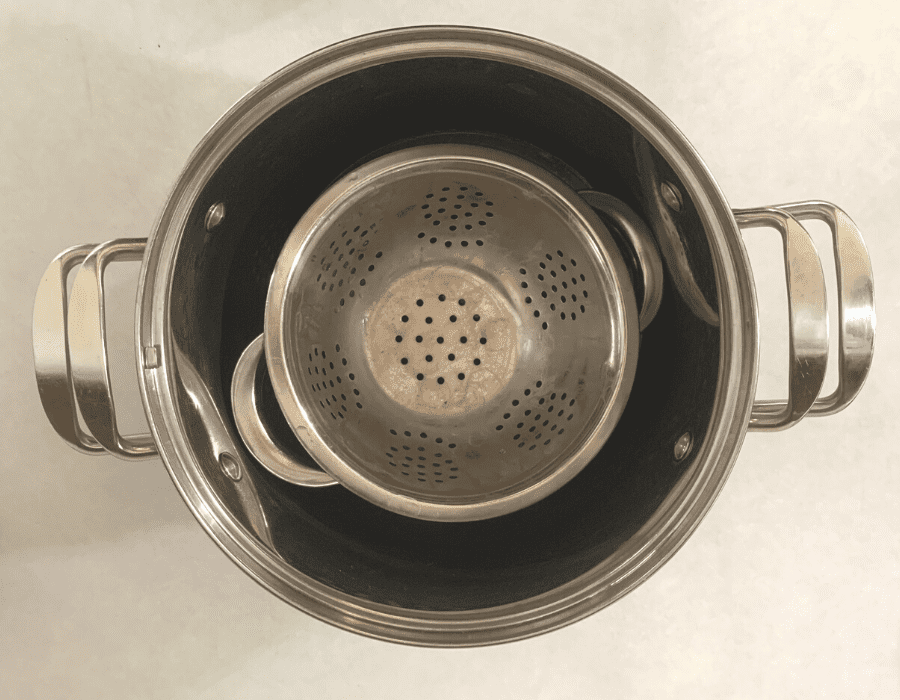 A stainless steel colander sitting inside a large stainless steel pot, sitting on a kitchen counter.