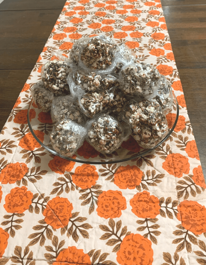 Popcorn balls wrapped in plastic wrap on a glass platter on a table.