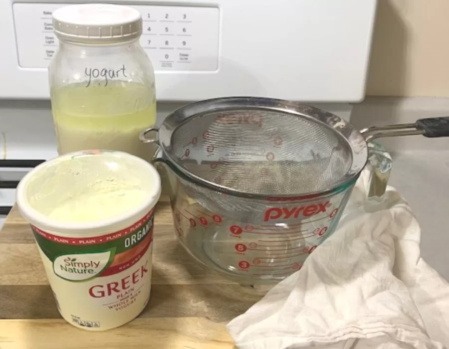 Homemade yogurt and store bought yogurt next to a large measuring cup with fine mesh sieve sitting on top.