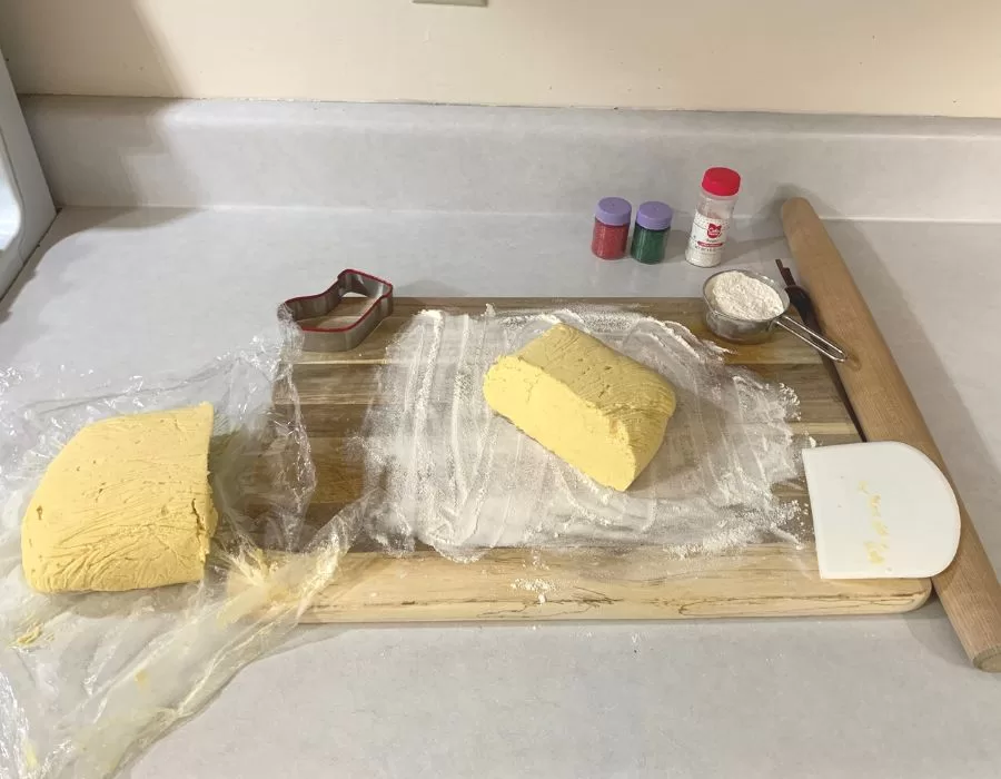 Cream cheese cookie dough cut in half on a floured wooden cutting board.