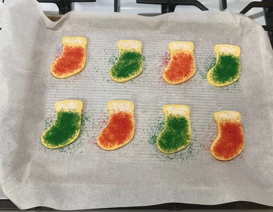 Sugar cookies in the shape of Christmas stockings with red, green, and white sprinkles on top.