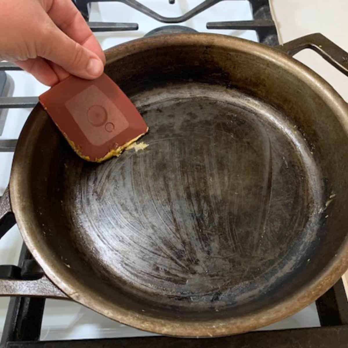 Woman scraping out a cast iron skillet using a pan scraper.