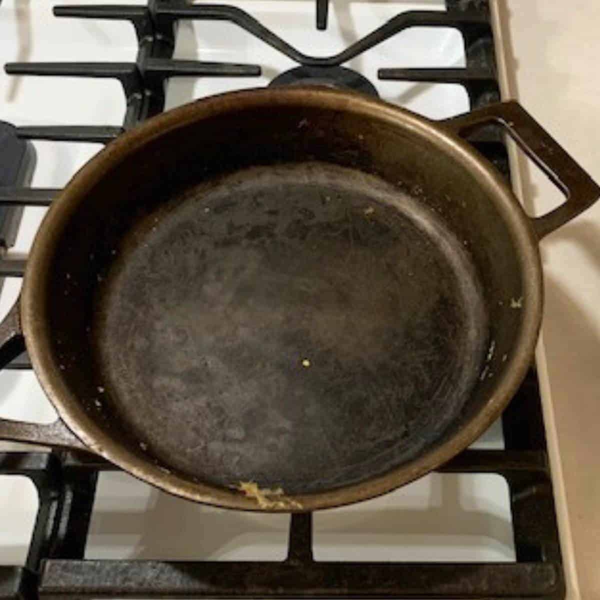 A dirty cast iron skillet sitting on top of a white gas stove.