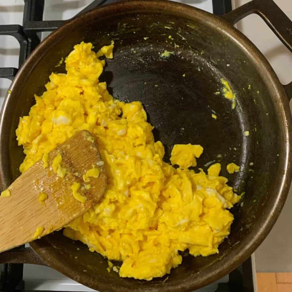 Woman cooking scrambled eggs in a cast iron skillet on top of a white gas stove.