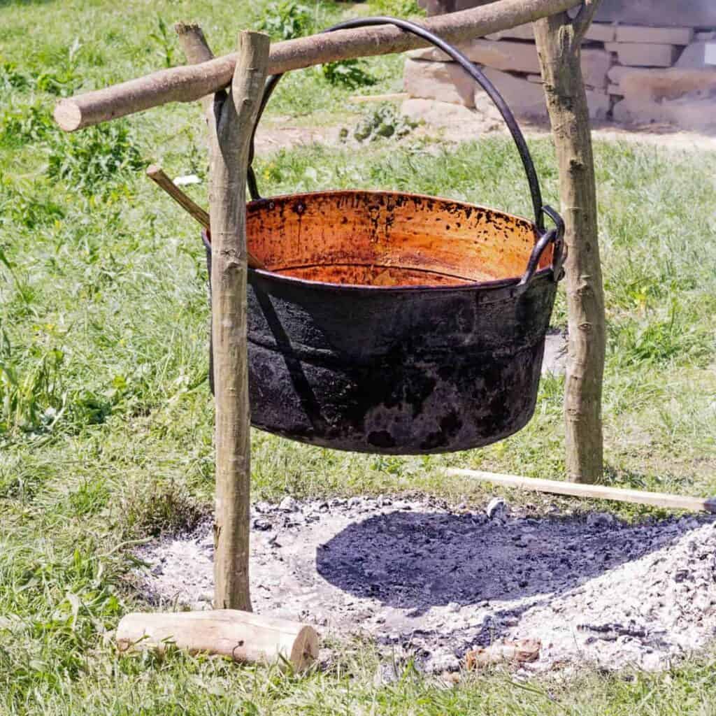 Hanging cast iron pot over a fire outside.