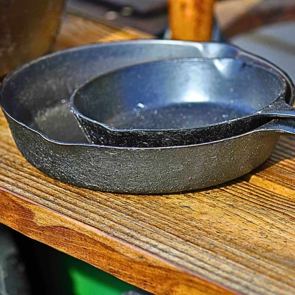 Two damaged cast iron skillets from a thrift store sitting on a wood board.