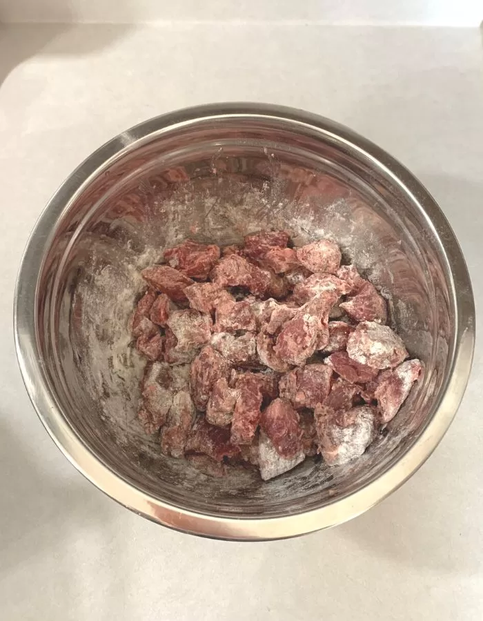 Beef stew meat covered in flour inside a mixing bowl.