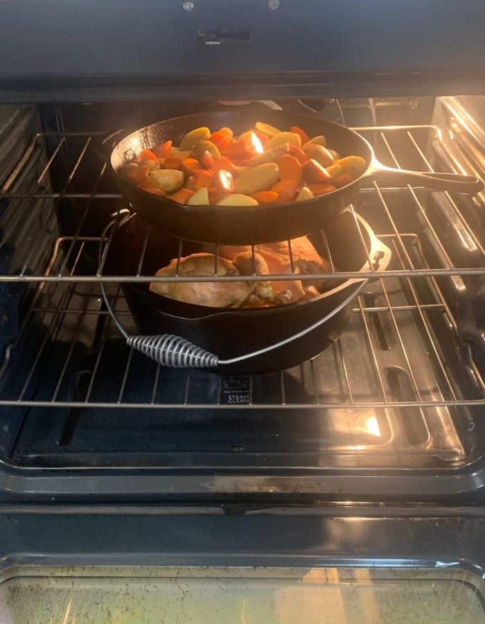 Chicken in a cast iron Dutch oven and potatoes and carrots in a cast iron skillet inside an oven.