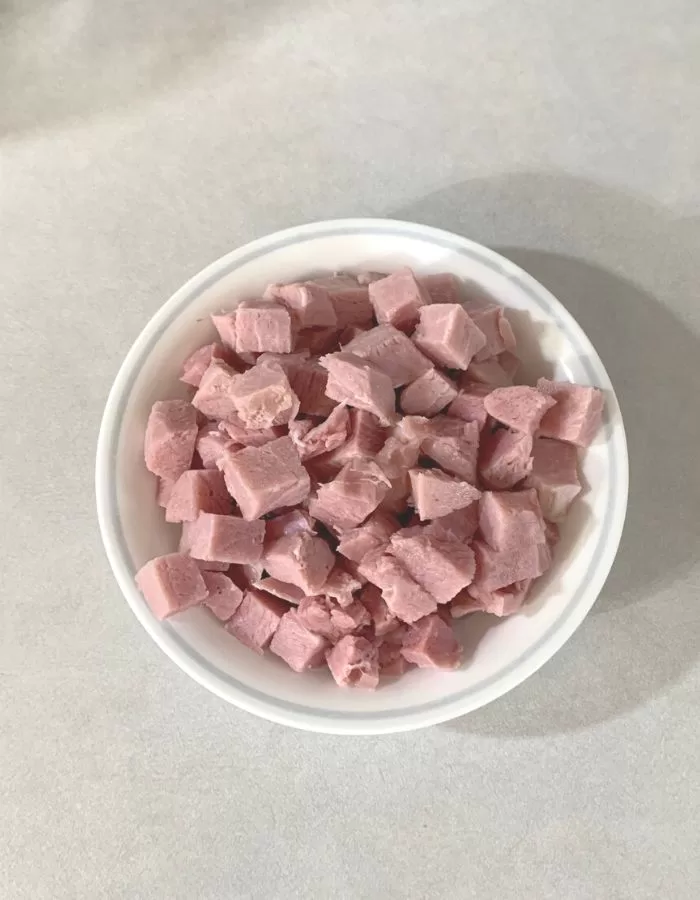 A ham steak cut into chunks in a white bowl on the counter.