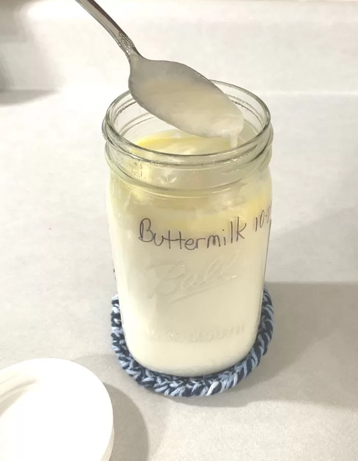 Homemade buttermilk in a quart mason jar. A spoon is dipped in and the buttermilk is dripping off in thick drips.