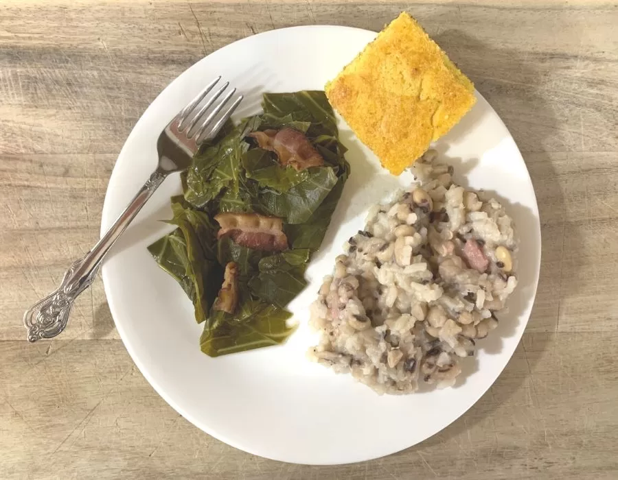 Southern pinto beans and collard greens on a white plate with yellow cornbread. Southern black eyed peas and collard greens.