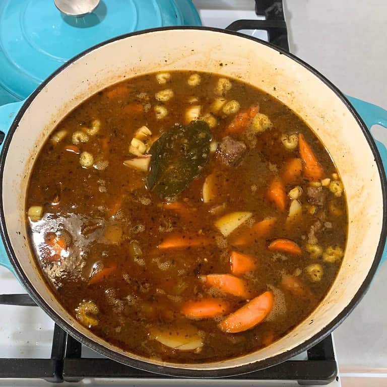 A turquoise enameled cast iron dutch oven on the stove filled with beef stew.