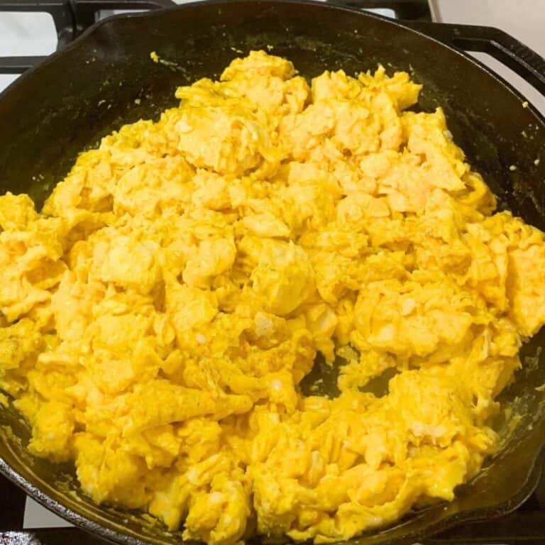 Scrambled eggs with milk in a cast iron skillet on a stove.