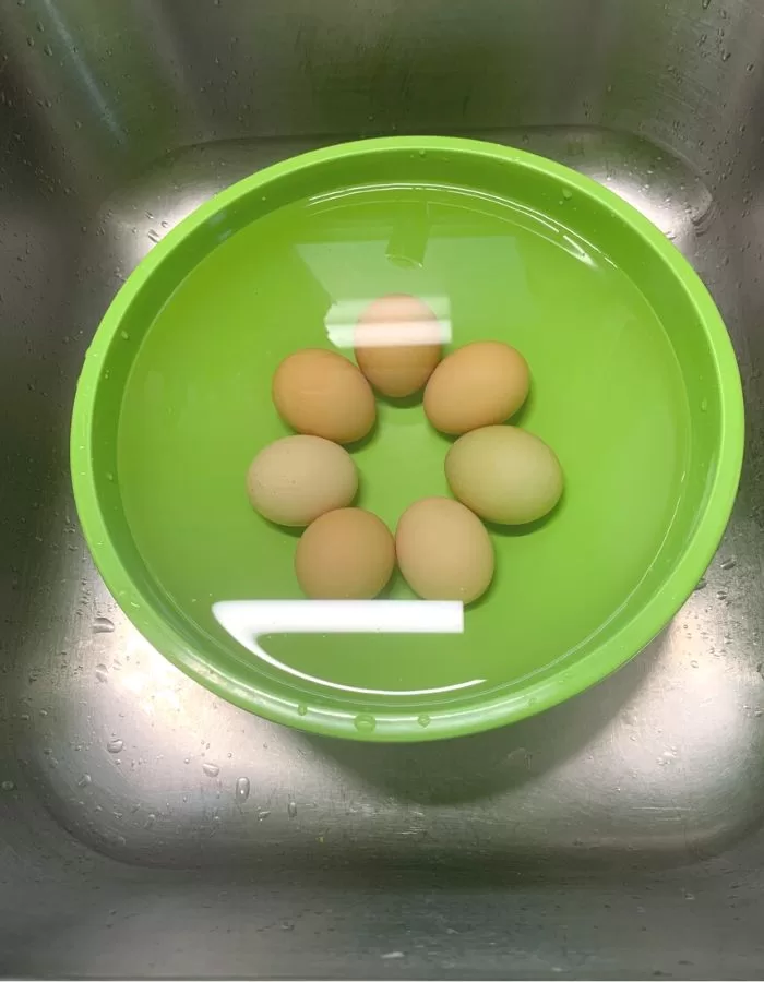 Eggs in a green bowl filled with water. The eggs sank to the bottom of the bowl.