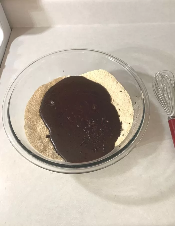 Large glass bowl on a counter with flour and sugar inside and melted chocolate poured on top.