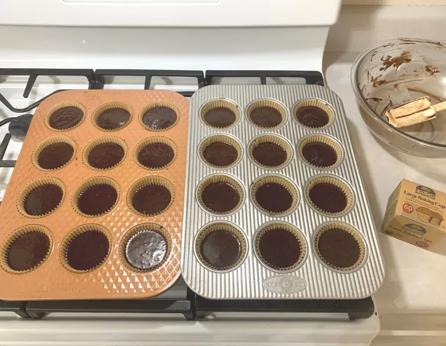 Two muffin pans lined with parchment paper with uncooked chocolate cupcake batter inside.